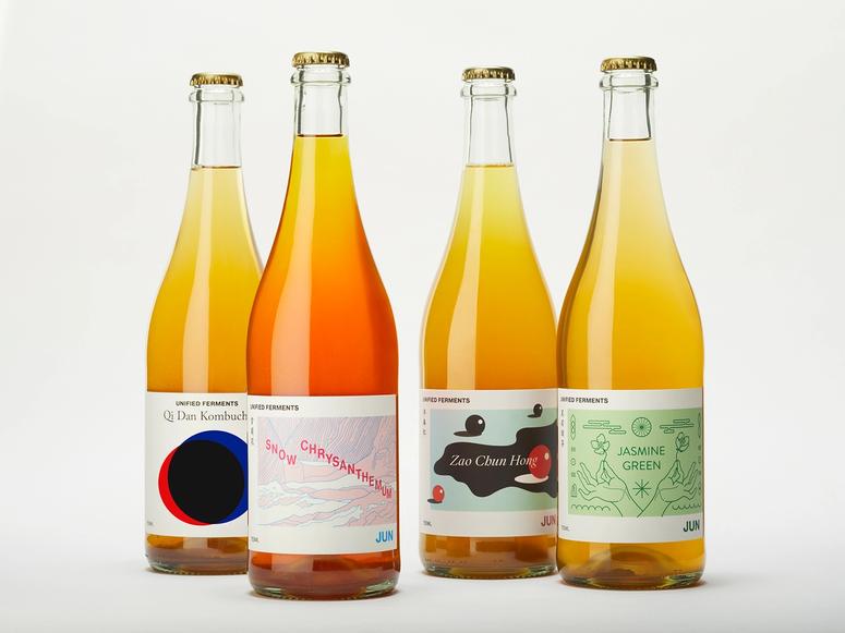 Four yellow and orange bottles of Unified Ferments teas on a white background.