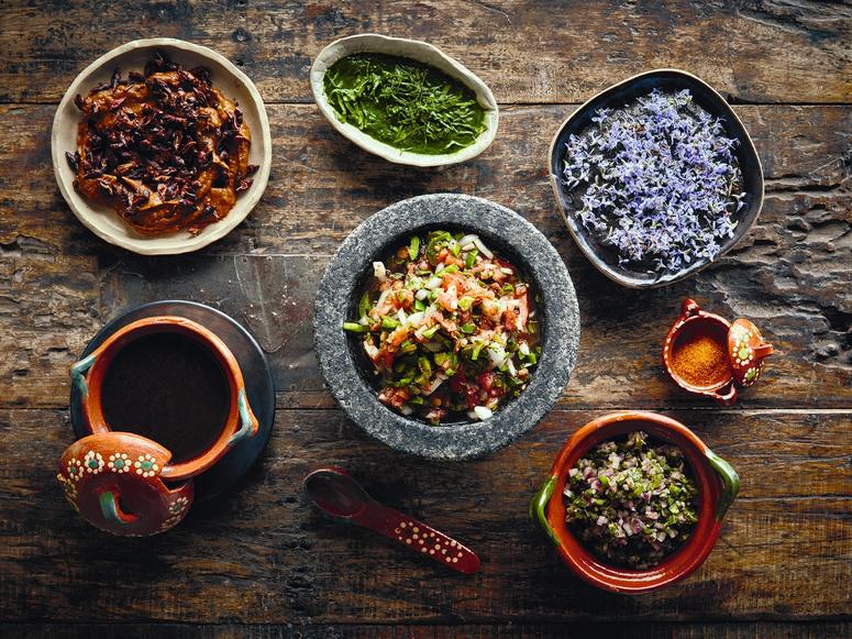 An arrangement of colorful dishes in stone and clay bowls on a wood table.