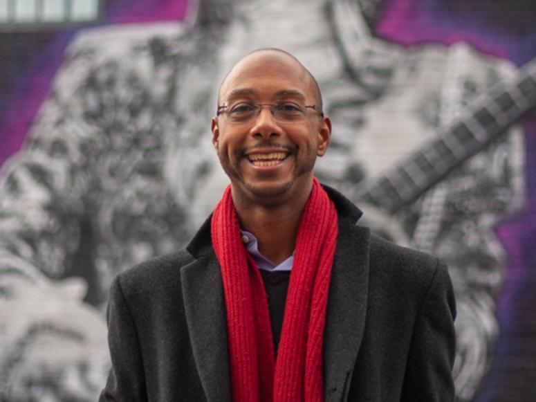 Author and scholar Elliott H. Powell with a red scarf in front of a mural.