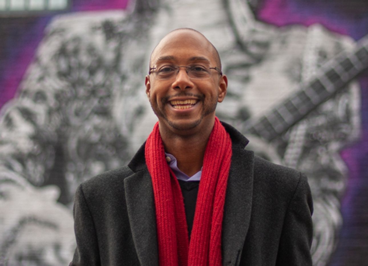 Author and scholar Elliott H. Powell with a red scarf in front of a mural.