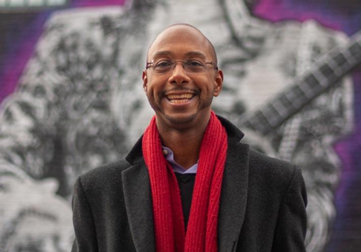 Author and scholar Elliott H. Powell with a red scarf in front of a mural.