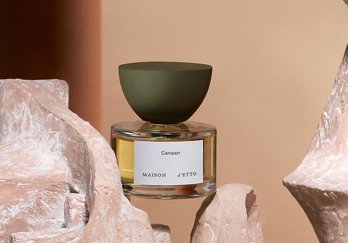 A sculptural bottle of perfume is balancing between two pieces of carved stone.
