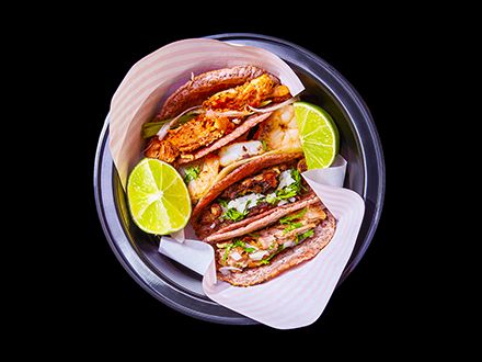Four tacos flanked by slices of lime.