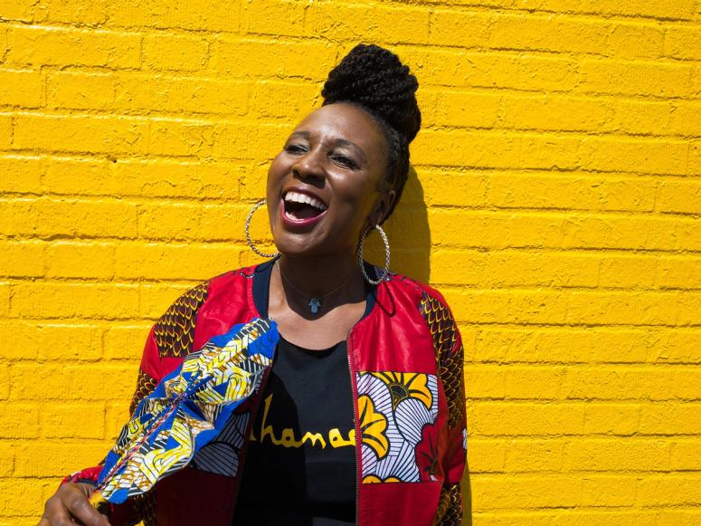 Toni Blackman laughing on a yellow brick background.