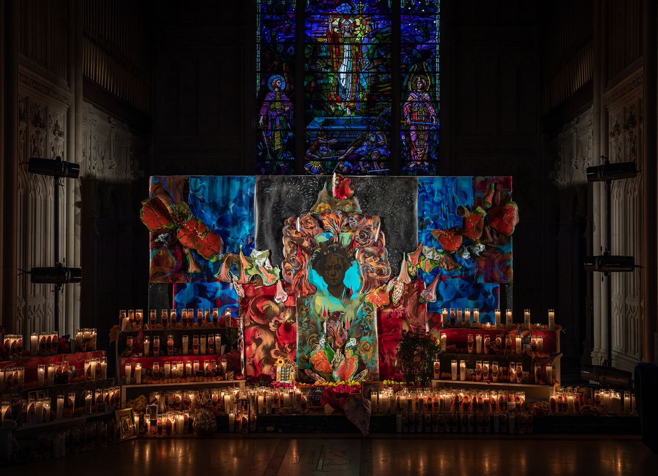 A church with stained glass window and rows of lit candles