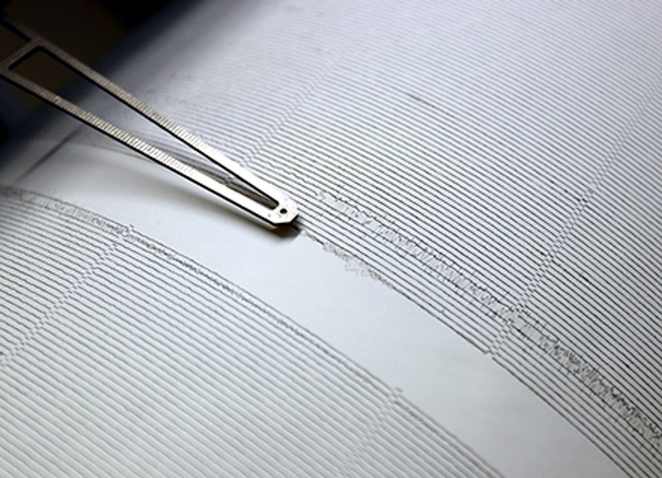 A seismograph needle drawing a black line across white paper.