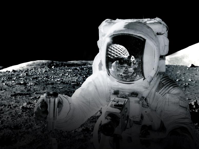 An astronaut on the moon, with a dome reflected in their visor.