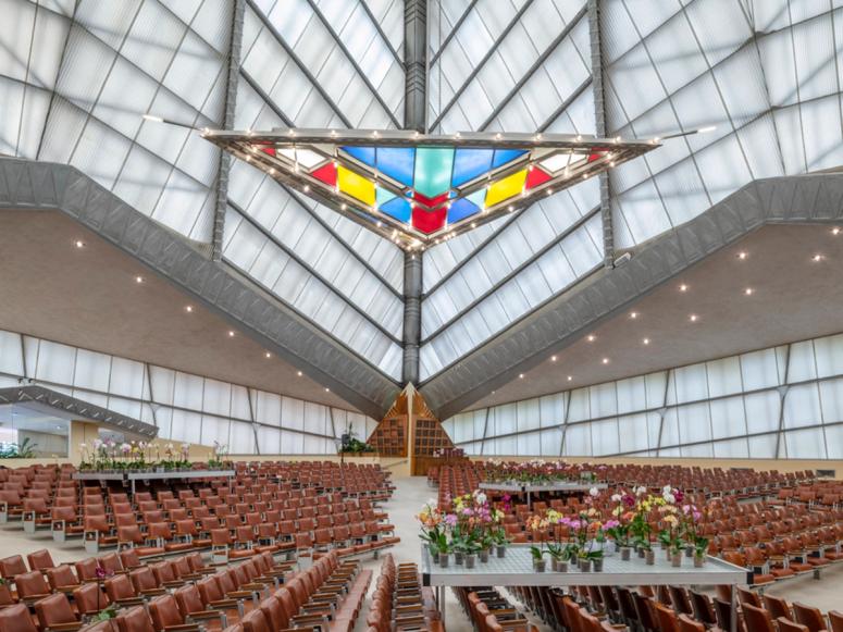 A large, open synagogue interior with a stained glass triangular chandelier.