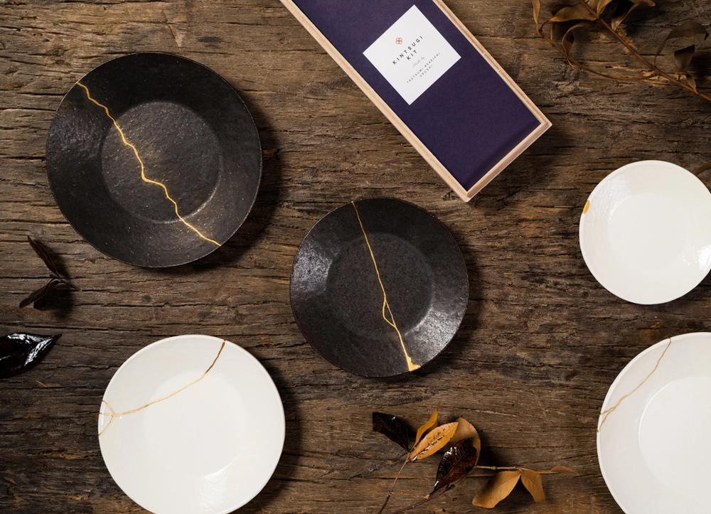 A kintsugi kit on a wooden table, next to several repaired plates.