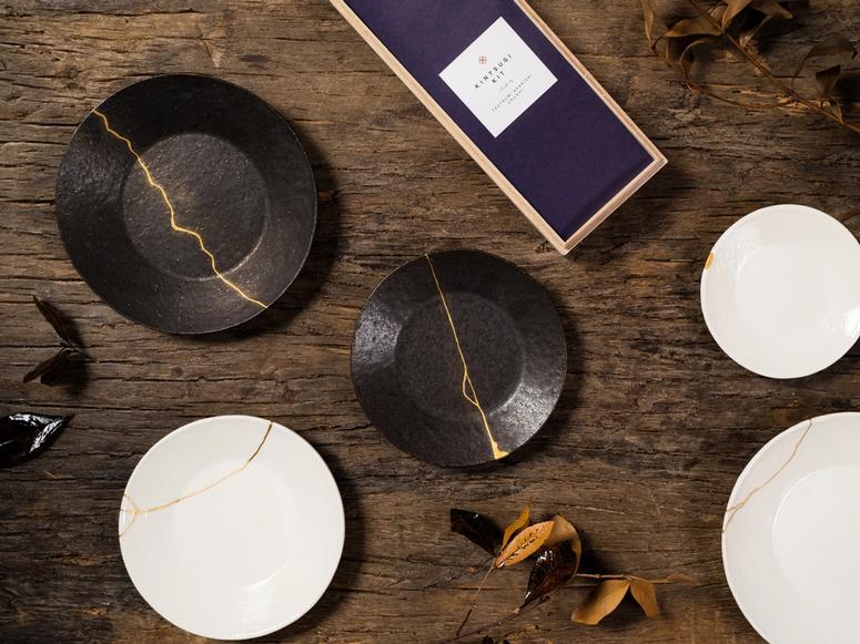 A kintsugi kit on a wooden table, next to several repaired plates.