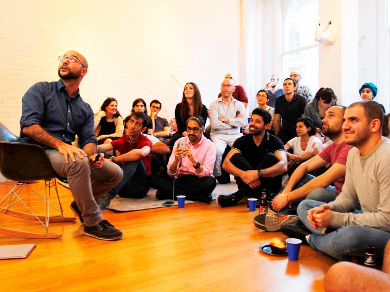 Mikey Muhanna sitting in a chair before a large group of presentation attendees, all looking at a presentation.