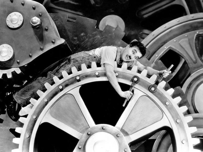 Charlie Chaplin riding the gears of a massive machine.