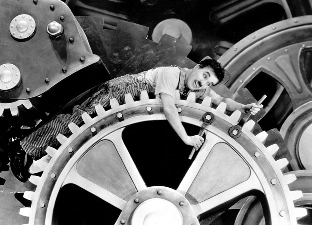 Charlie Chaplin riding the gears of a massive machine.