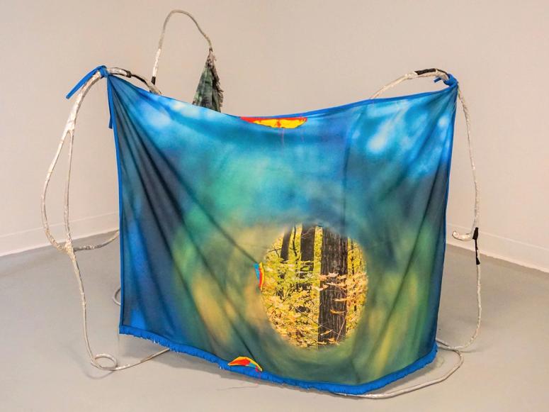 A blue printed textile hung with aluminum wire in an art gallery.