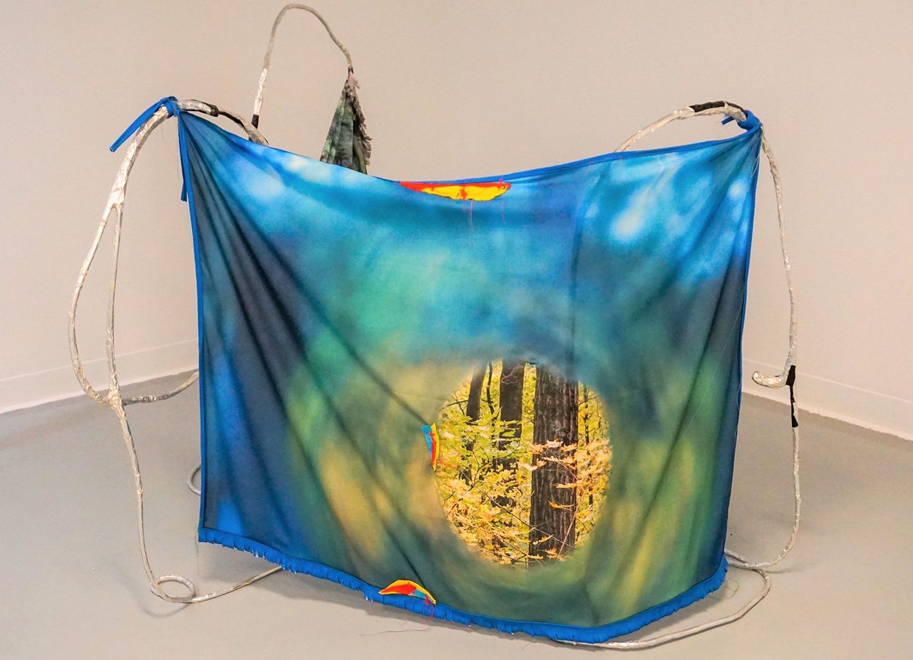 A blue printed textile hung with aluminum wire in an art gallery.