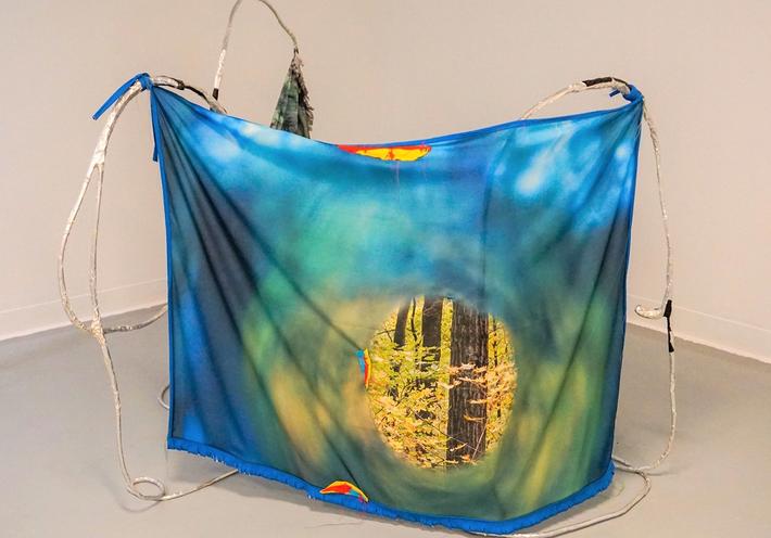 A blue printed textile hung with aluminum wire in an art gallery.