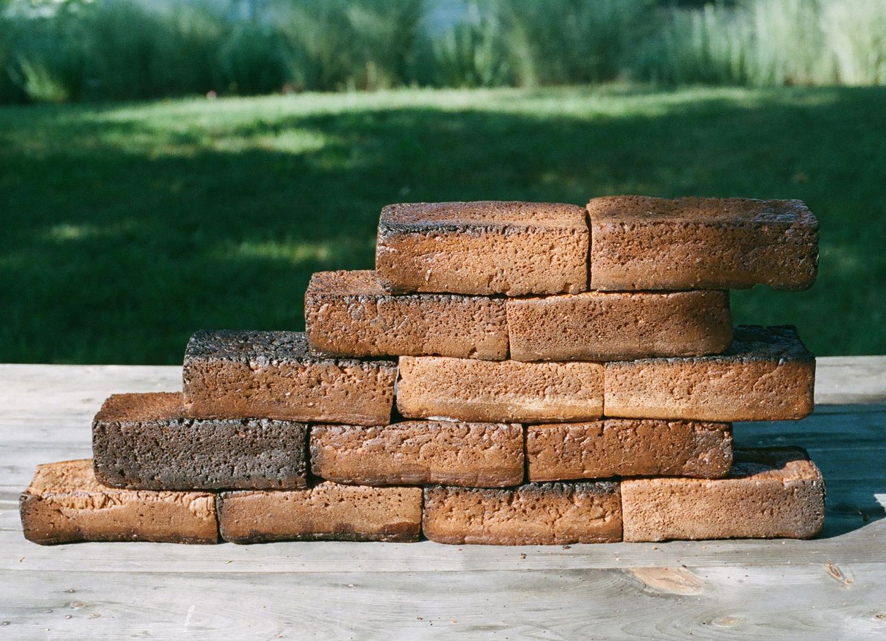 A stack of brick-like bread loaves with a green lawn in the background.
