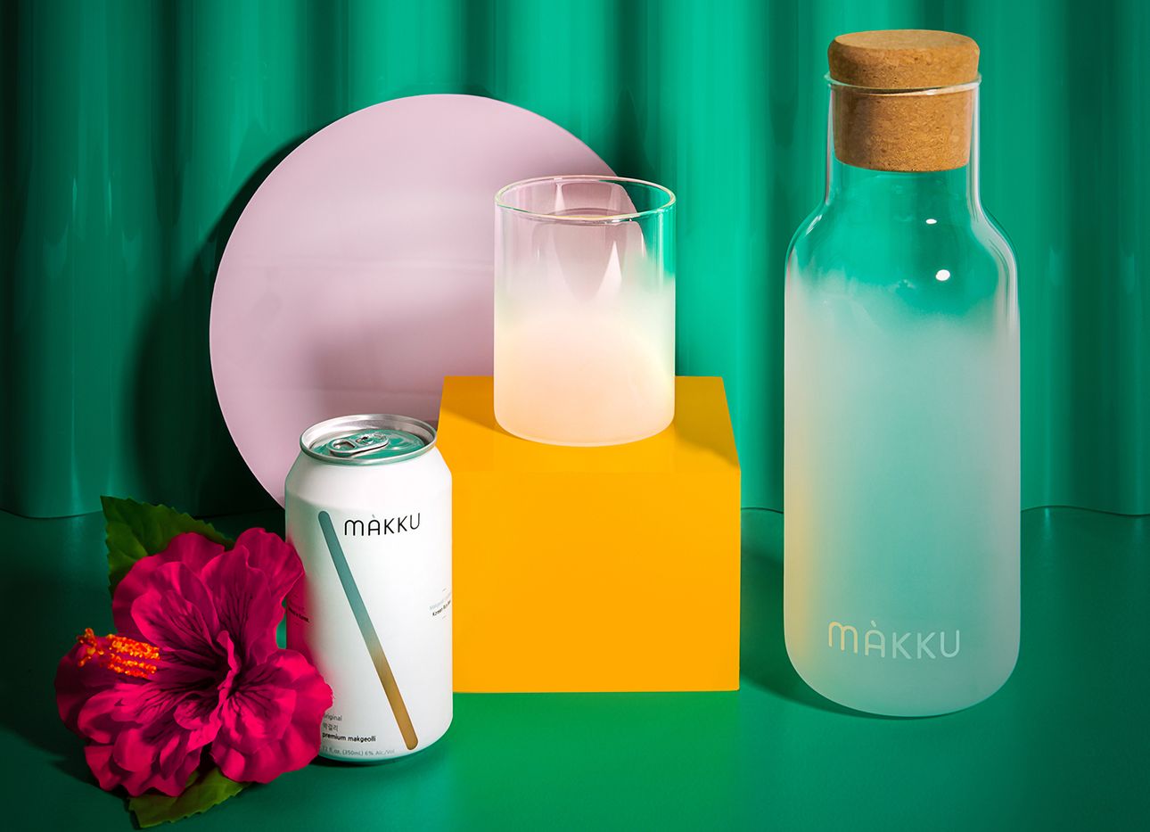 A carafe, glass, and can of Makku on a green backdrop.