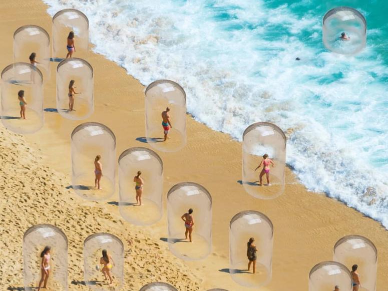 Various people encased in glass bubbles stand on the beach near the ocean