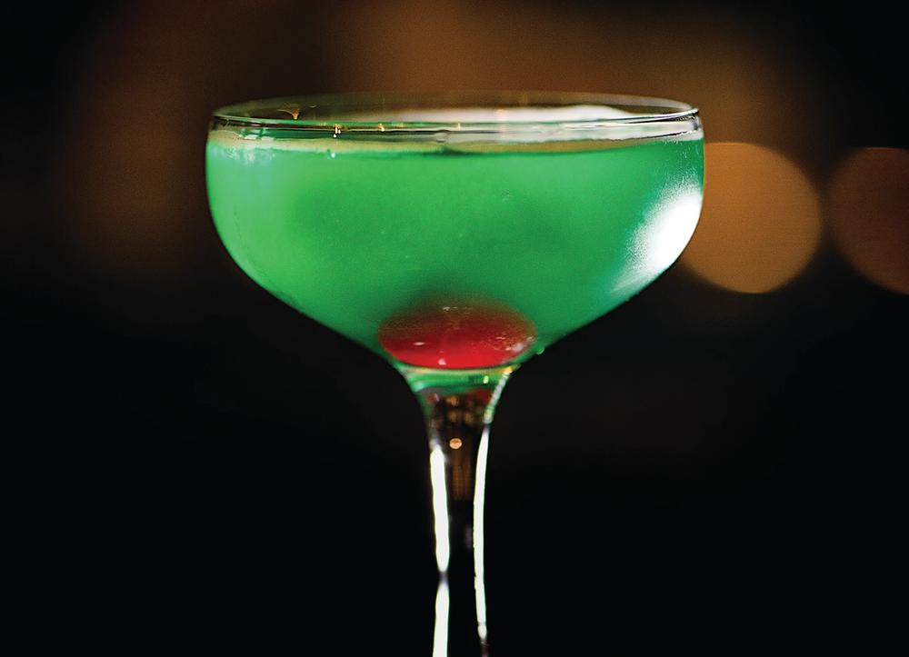 A martini glass with green drink and cherry inside