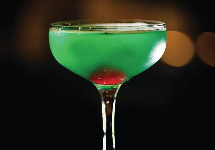 A martini glass with green drink and cherry inside