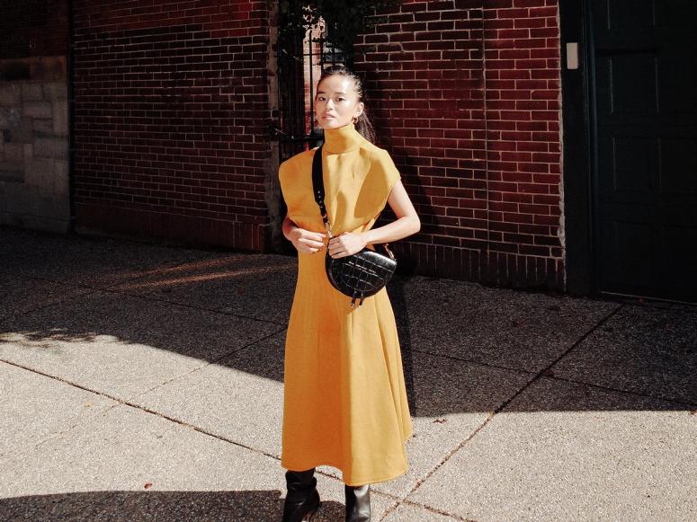 Olivia Lopez in a yellow dress, with a black leather handbag.