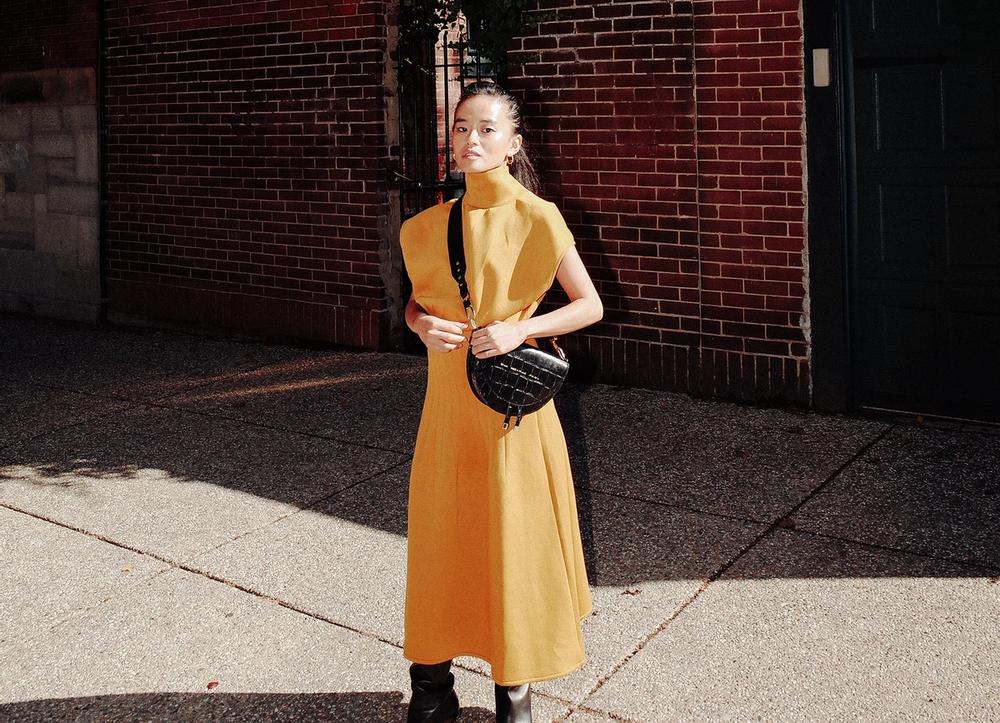 Olivia Lopez in a yellow dress, with a black leather handbag.