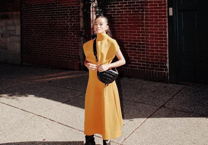 Olivia Lopez in a yellow dress, with a black leather handbag.