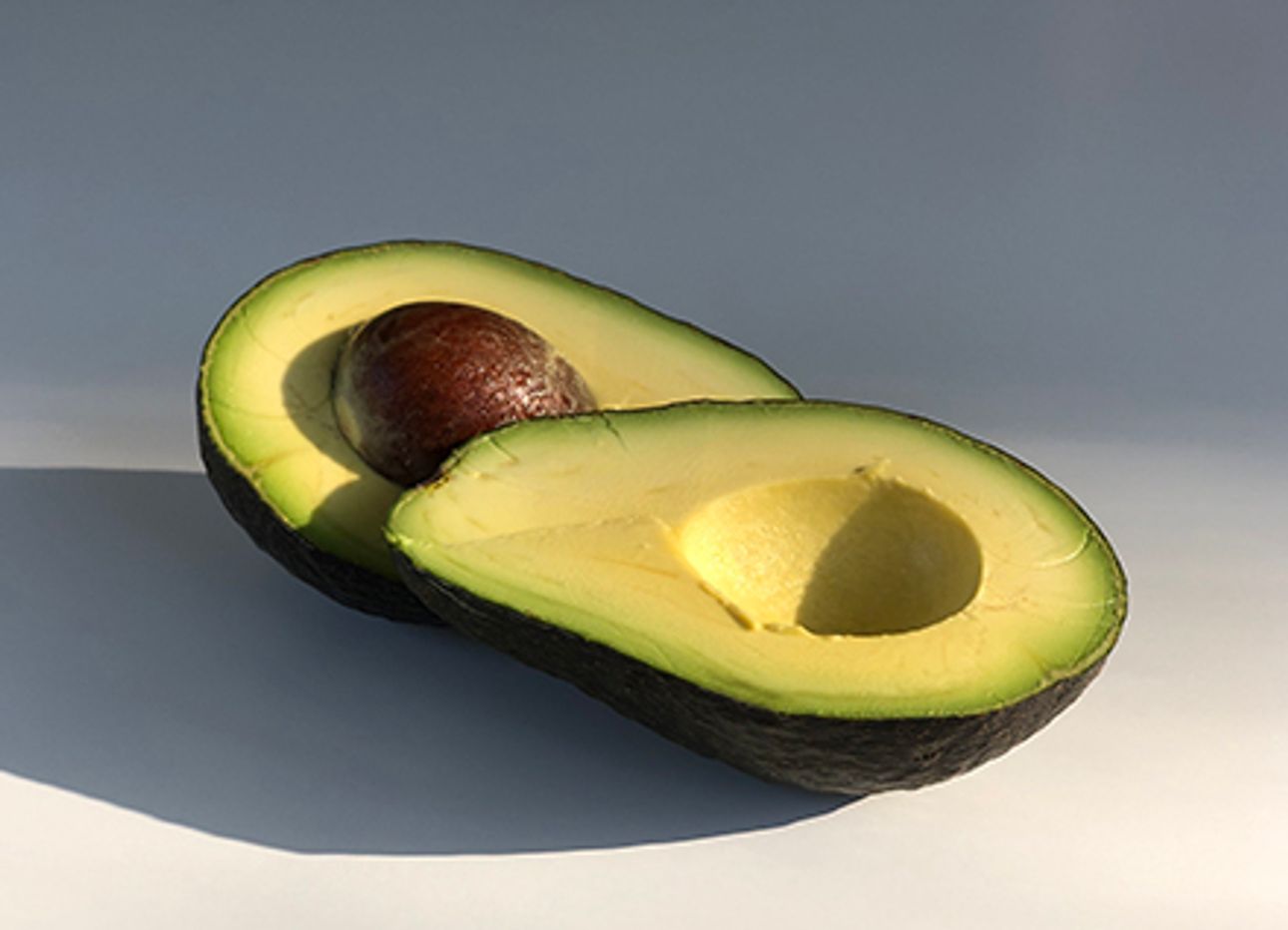 A split avocado in bright, moody lighting.