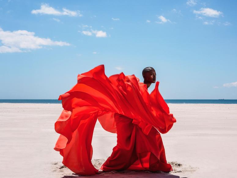 A photograph of a woman in a bright red dress on the beach.