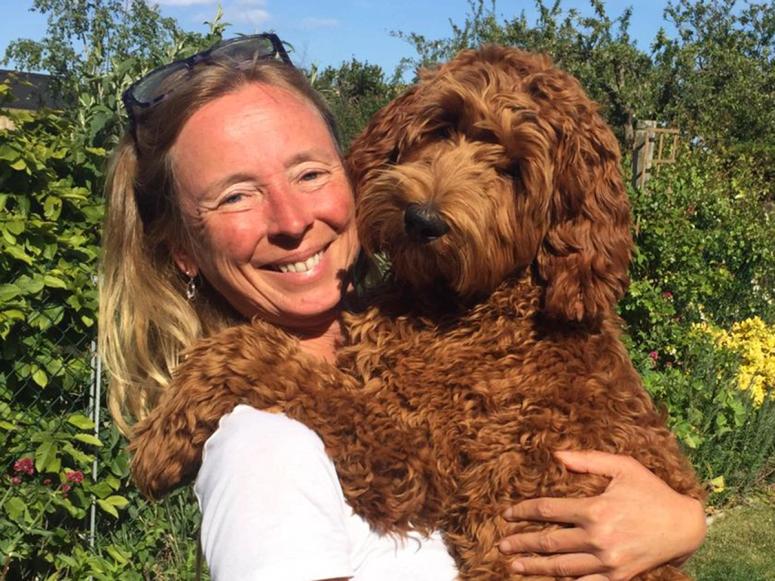 Dr. Kate McLean smiles and holds her dog in a garden.