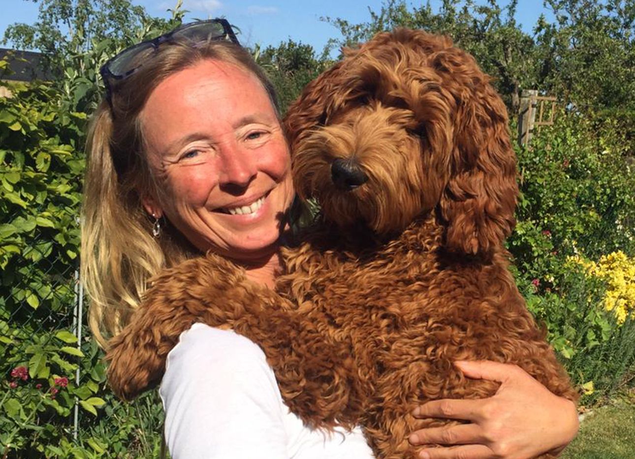 Dr. Kate McLean smiles and holds her dog in a garden.