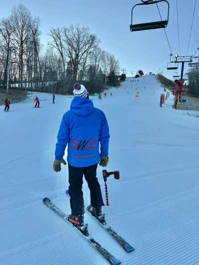 Skier in a SWAT jacket at the top of a run beneath the chairlift