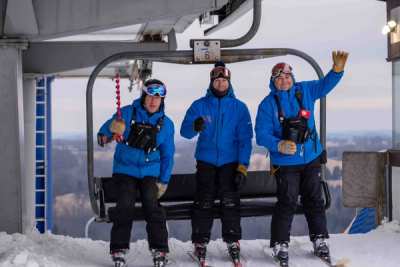 Three coaches riding the chairlift, one waving at the camera