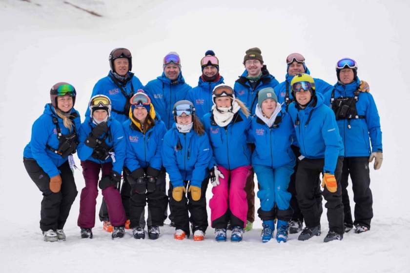 Full team group photo in blue SWAT jackets on the snow
