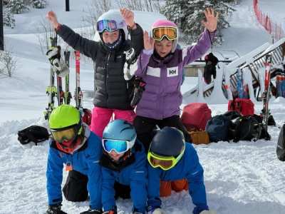 Young athletes in goggles piled together on the snow, waving