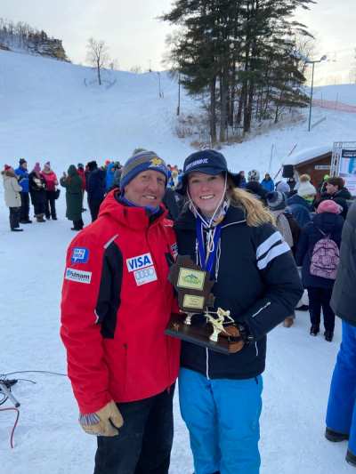 Coach and athlete holding a trophy in the crowd at the base area