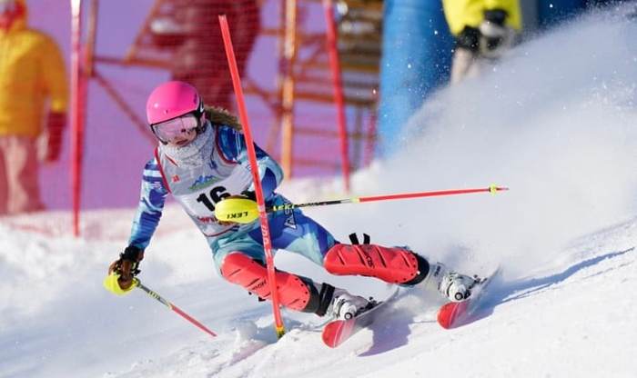 Racer in a pink helmet carving a slalom turn past a gate