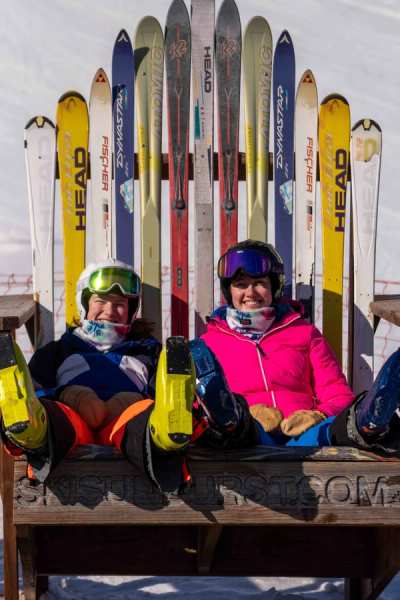 Two athletes sitting in front of a rack of race skis
