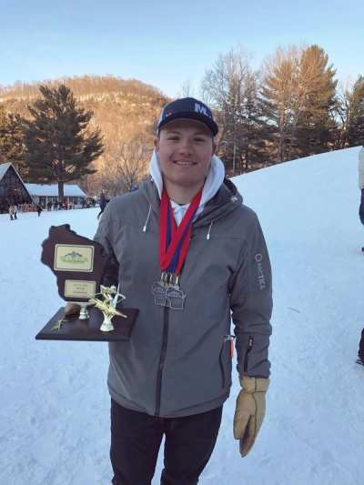 Coach holding a plaque and a set of medals outside at the hill