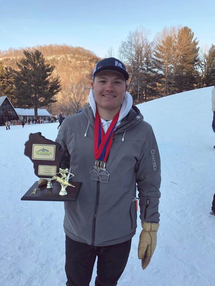 Coach holding a plaque and a set of medals outside at the hill