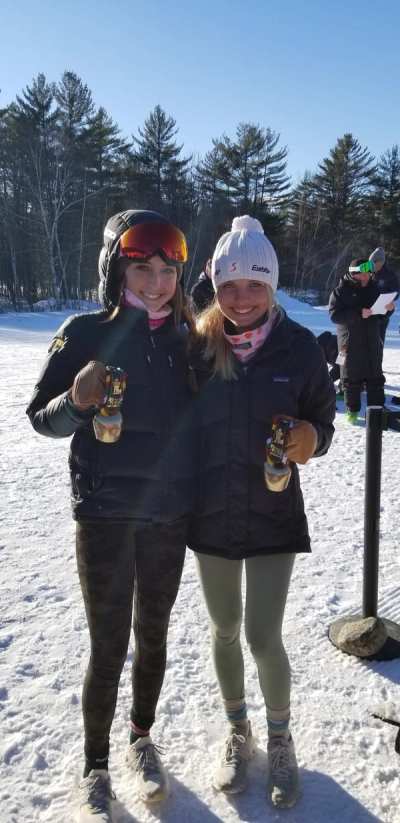Two athletes standing on the snow holding their medals