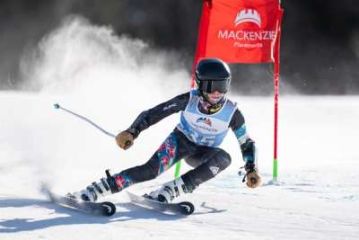 Racer carving hard past a red giant slalom panel, throwing snow