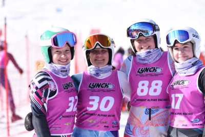 Four athletes in pink race bibs standing together at a competition