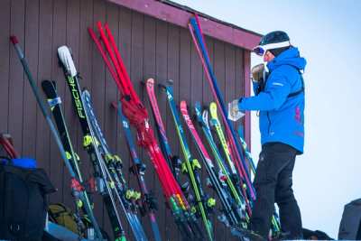 Coach beside a rack of race skis against a red lodge wall