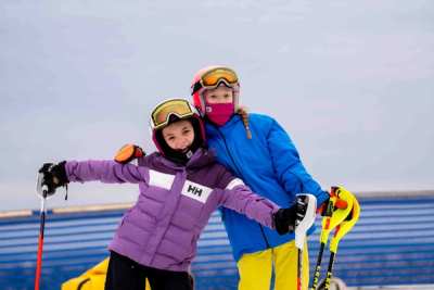 Coach and a young athlete on the snow with their arms out, laughing