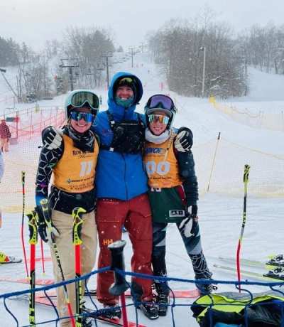Three racers in bibs standing arm in arm at the finish, gates behind them