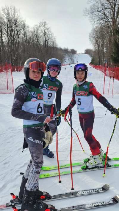 Three racers in numbered bibs standing together on the hill
