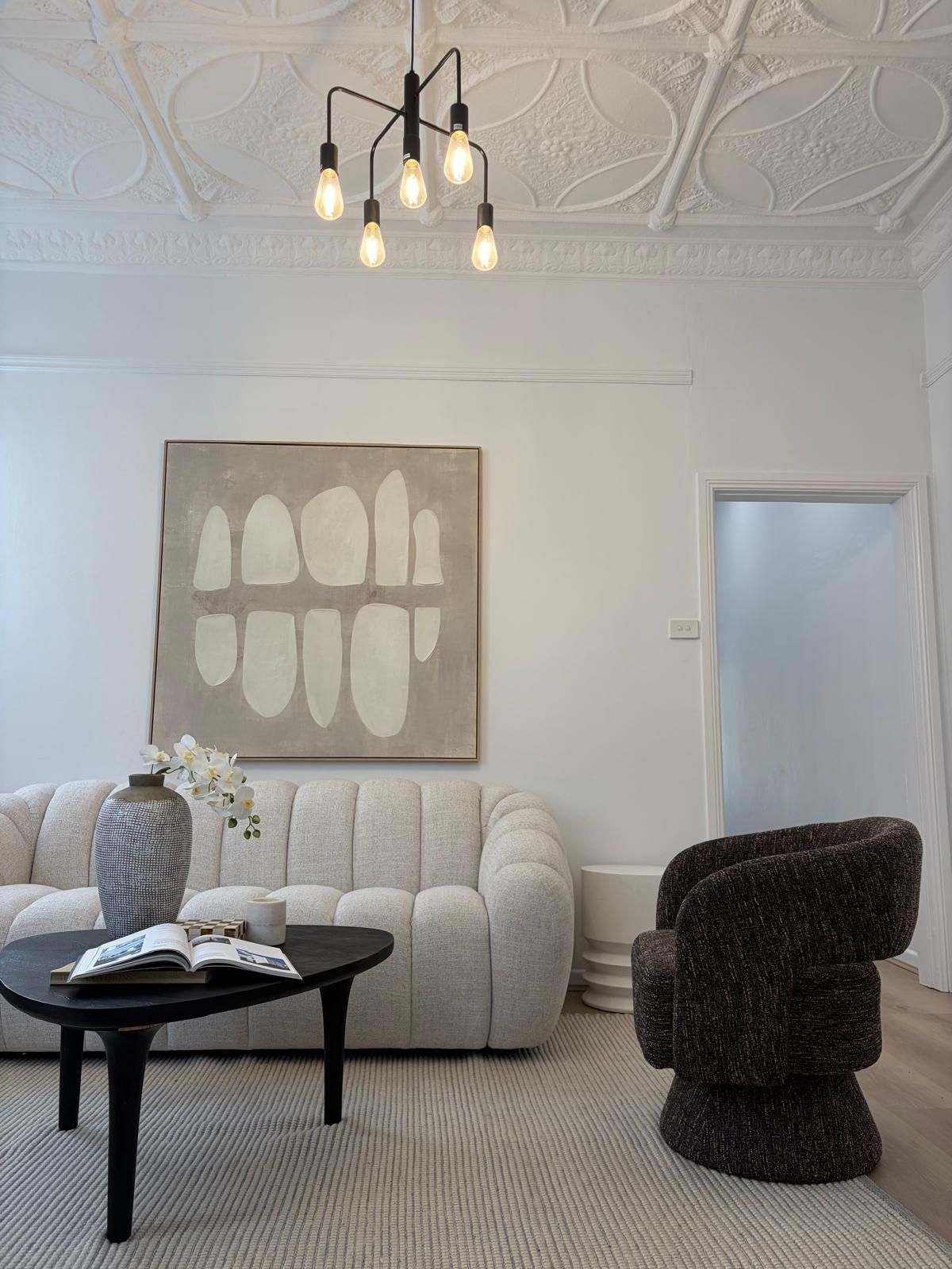 Dining room with a round table and cream boucle chairs, a round mirror above a black sideboard and a striped ceramic vase