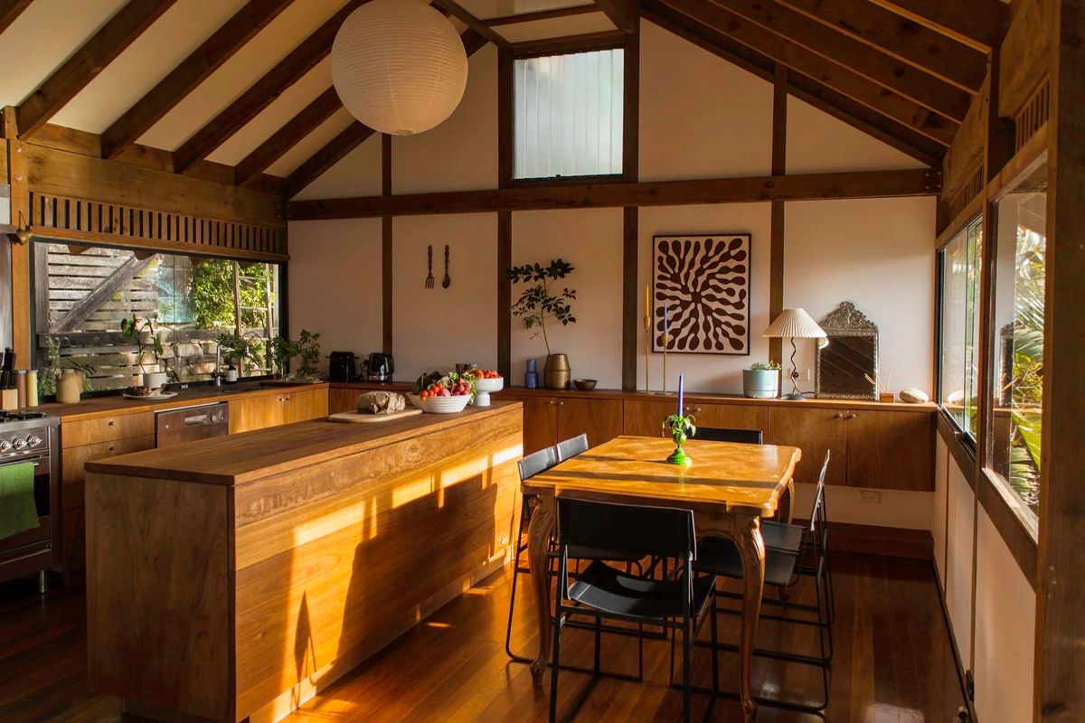 Open kitchen and dining space under a vaulted timber ceiling, with a paper lantern, wood island bench and a dressed dining table